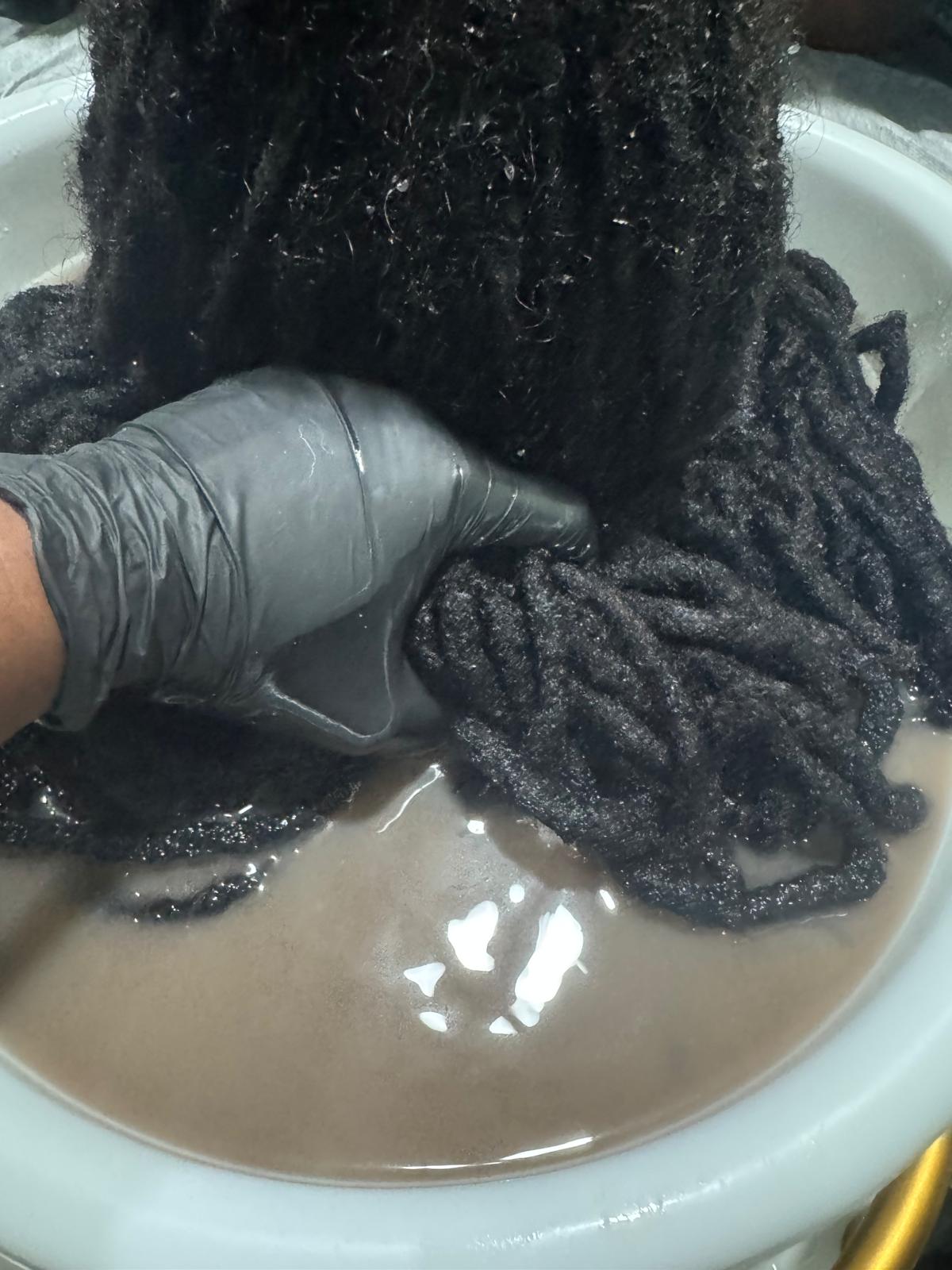 Locs being cleansed and detoxed in the treatment basin during a wellness-focused service.