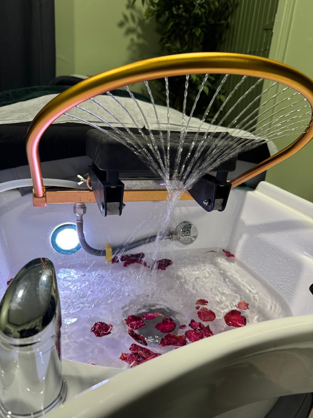 Flowing water arch over the treatment basin with rose petals for a calming head spa ritual.