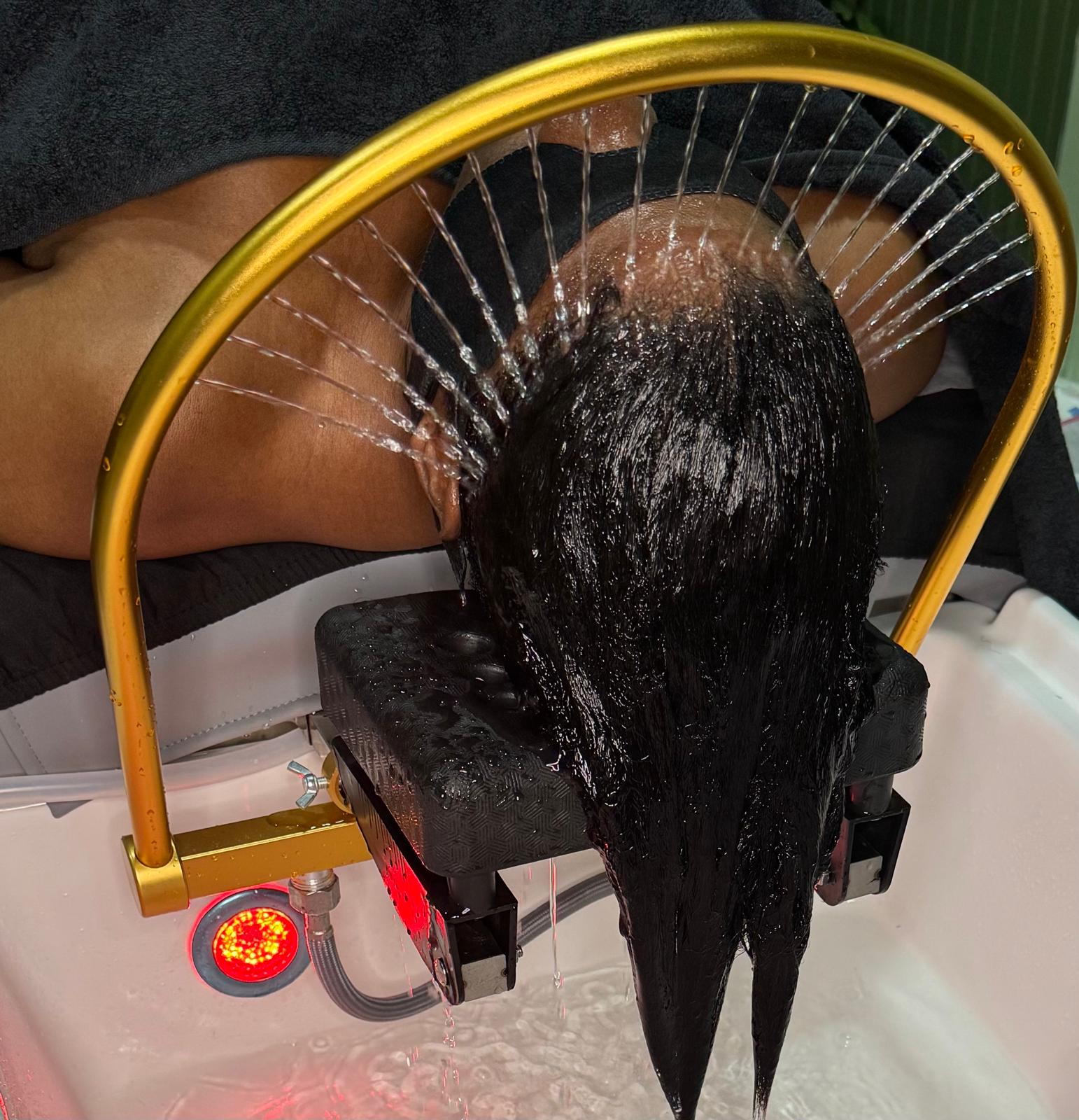 Dark hair flowing beneath the signature golden water arch during a soothing rinse.