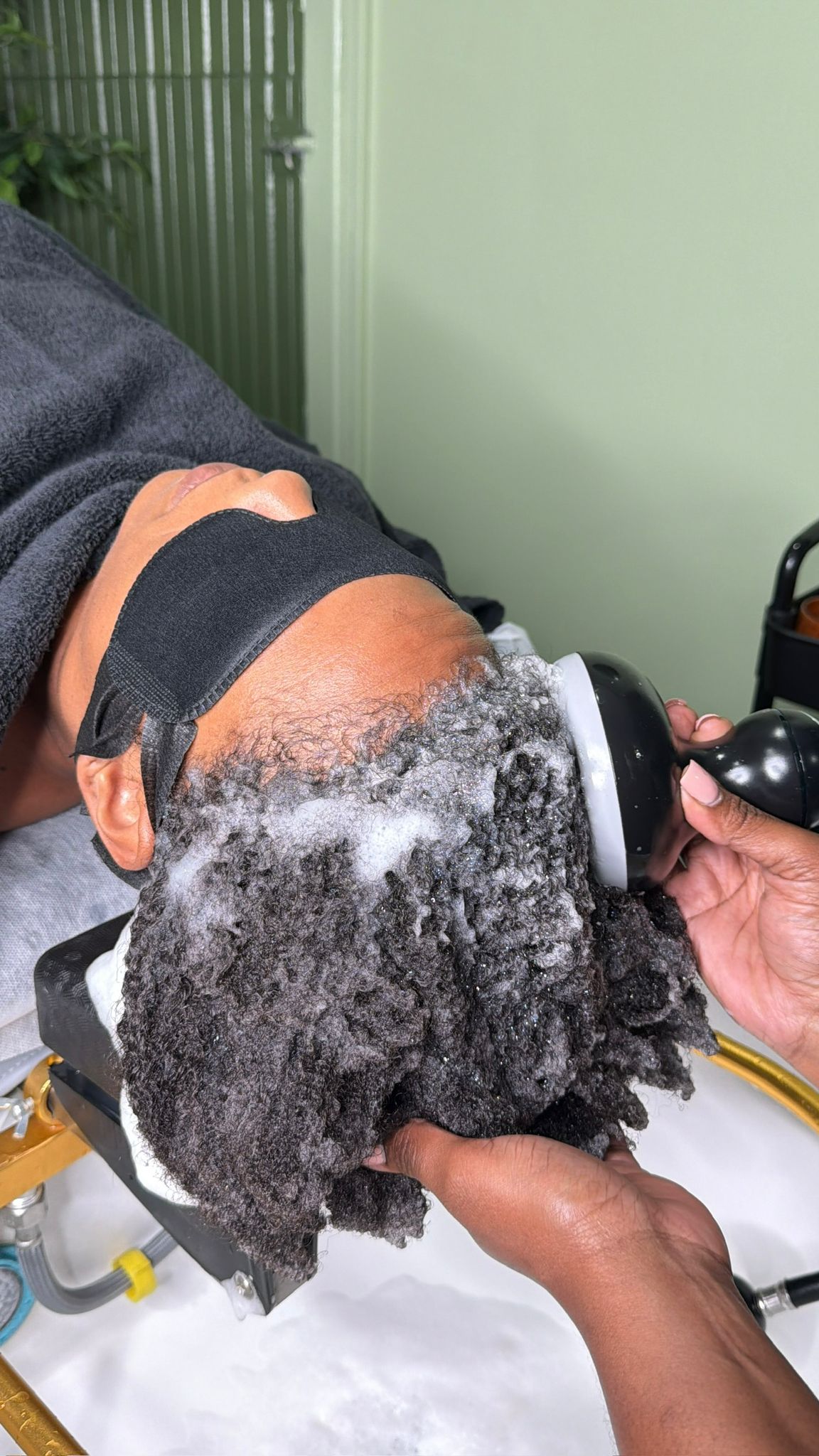 Therapist using a cleansing tool to work shampoo through natural hair at the Zen Den.